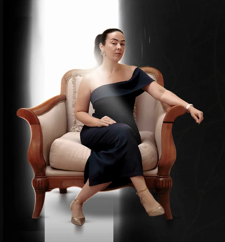 Aline Senatore sentada numa poltrona, sob um feixe de luz